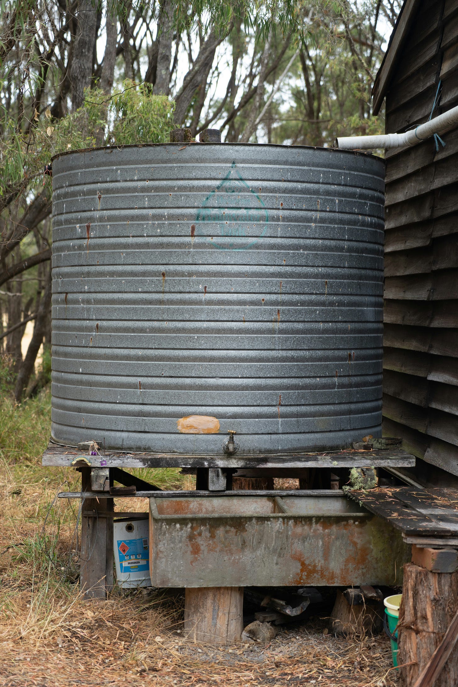 A large, round metal container sits atop a wooden stand. A rain pipe ends just above the container
