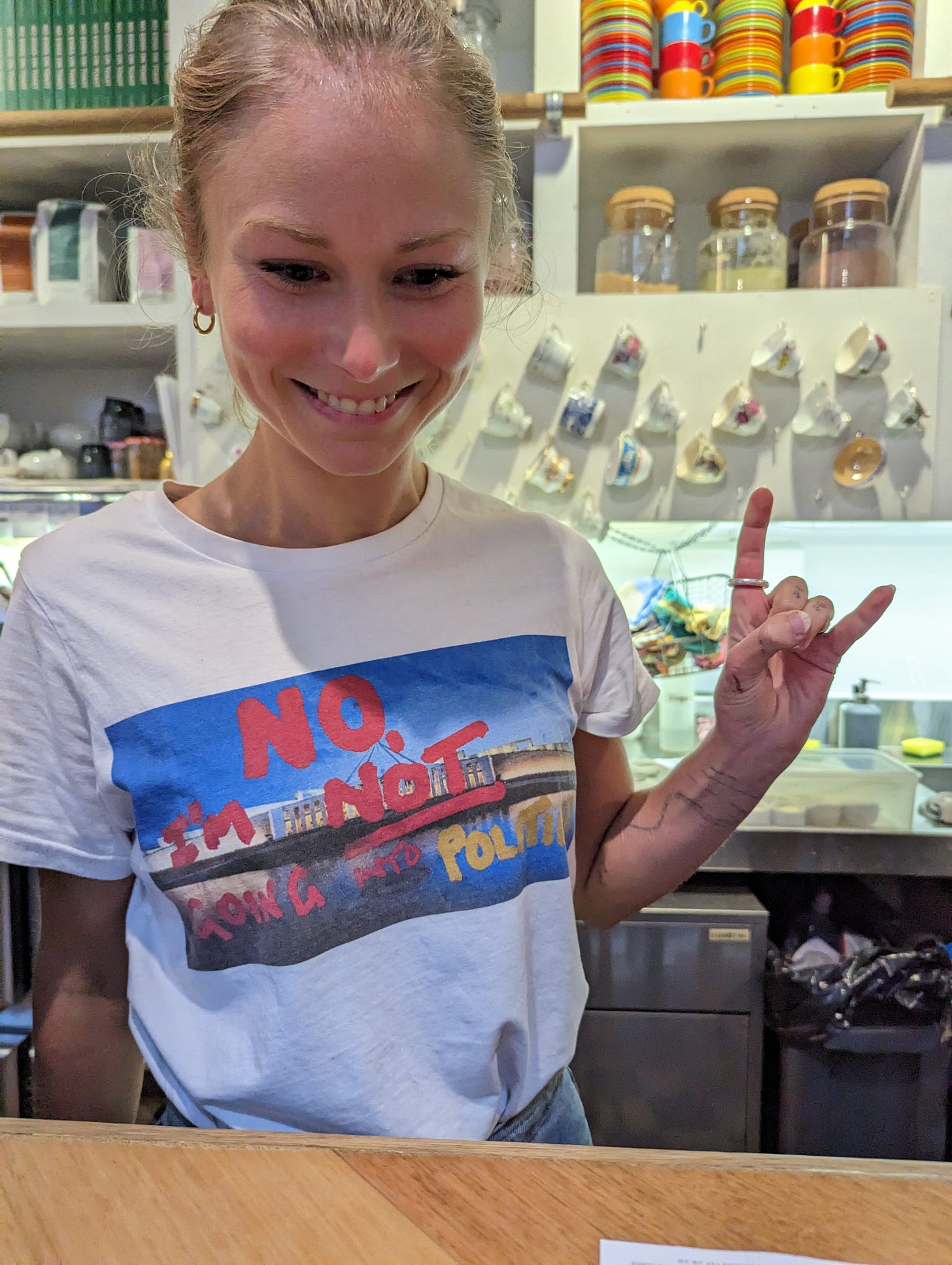 Grace Tame sits at table in a Melbourne Cafe. The shirt has  the words "No I'm Not Going Into Politics" 
