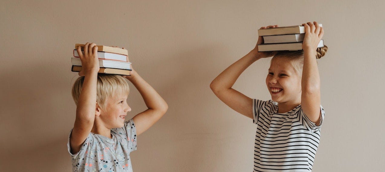 Two children standing with books on their heads, smiling
