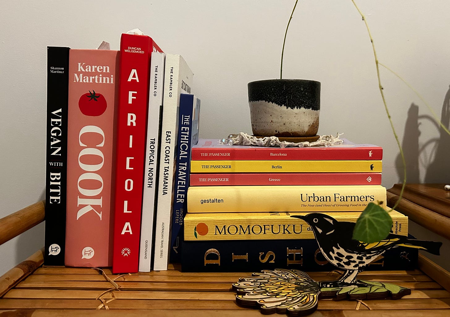 A stack of cookbooks and travel books, sitting on a bamboo shelf.