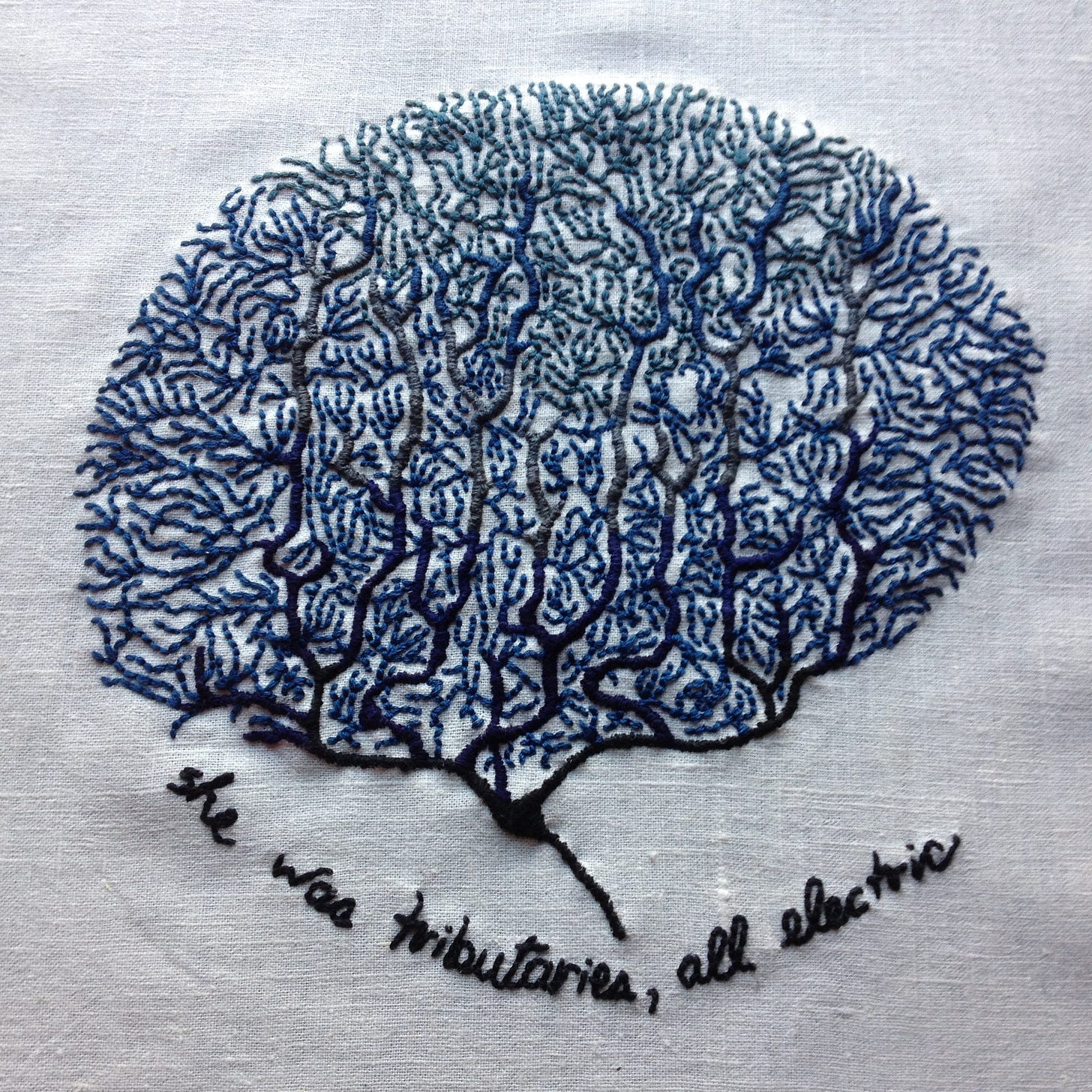 she was tributaries (2016)  An embroidery on bone white linen. There are many coral-like neurons in the vague shape of a brain embroidered in shades of blue. The bottom section is navy blue and transitions to a lighter blue at the top. The text at the bottom reads: she was tributaries, all electric.