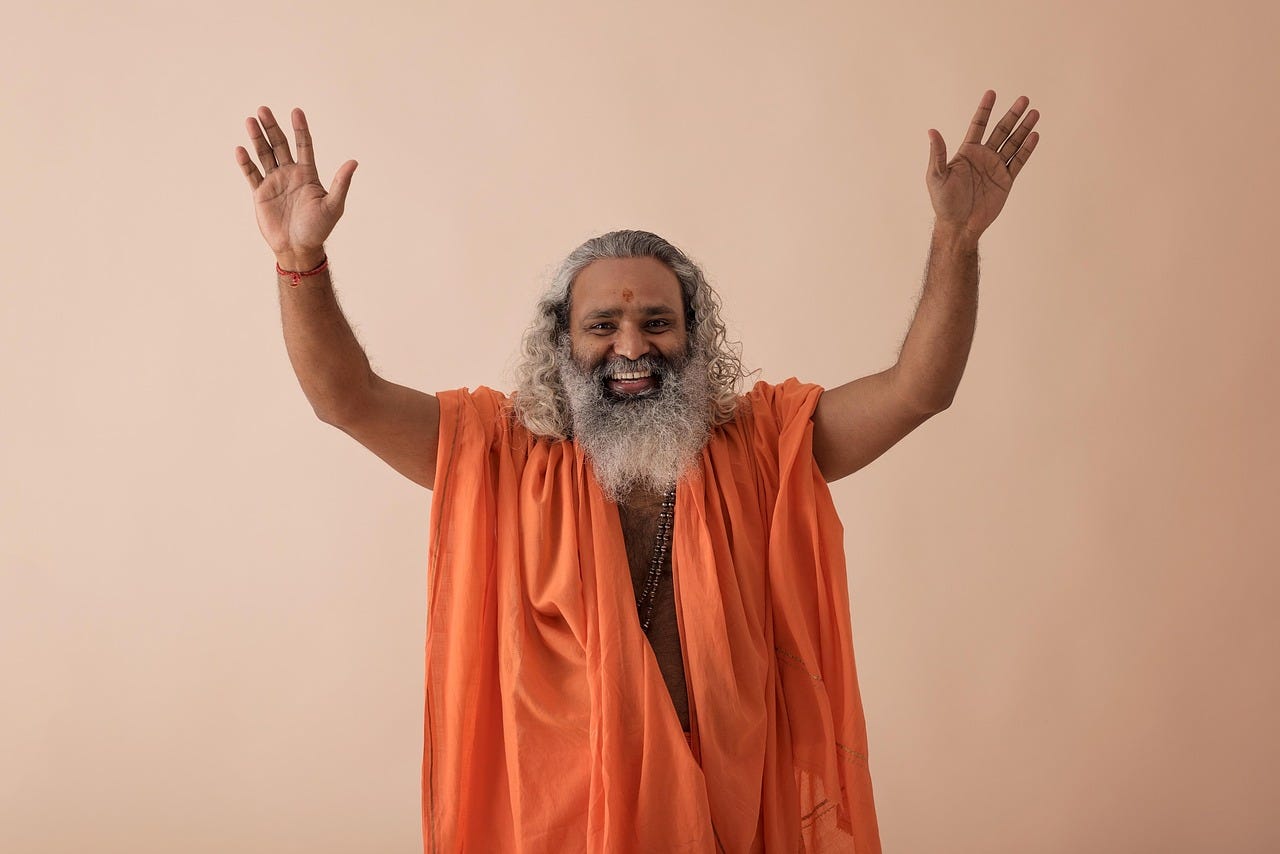 Swami wearing orange with his hands raised over his head, smiling Swami wearing orange with his hands raised over his head, smiling