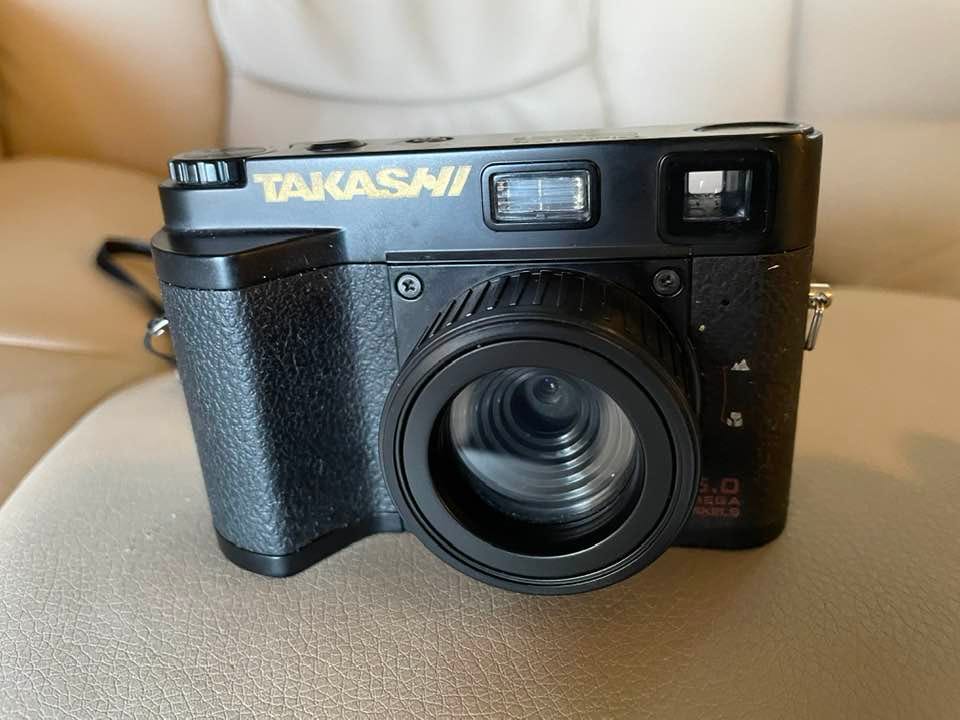 May be an image of camera and text that says 'TAKASHI'