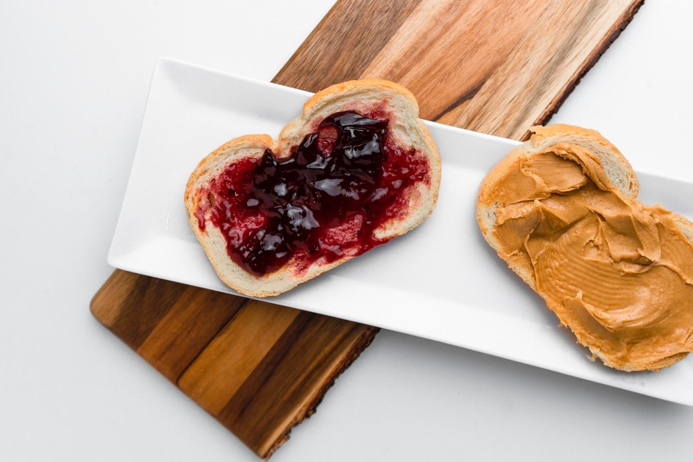 Two pieces of bread on a white plate, one with peanut butter, the other with jelly