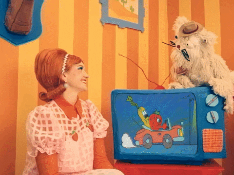 GIF that says "buckle up buttercup" with a muppety character on top of a felt TV, talking to a 50s styled woman in an apricot-colour striped room