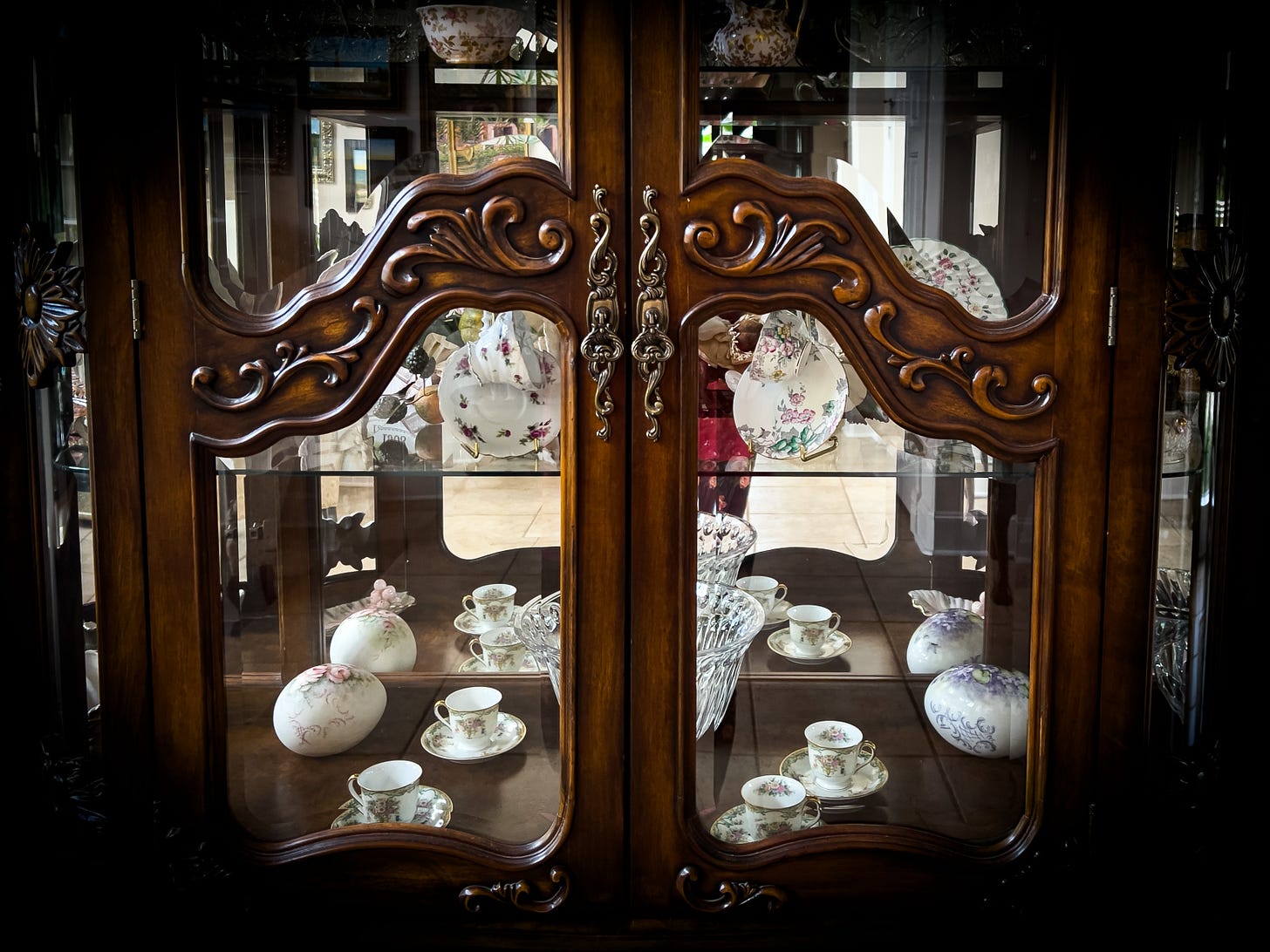 A view into an antique curio cabinet with tea cups, porcelain, and crystal bowls