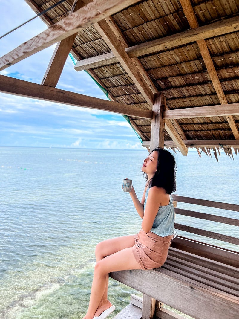 Asian girl holding a coffee mug in a stilted nipa hut by the sea