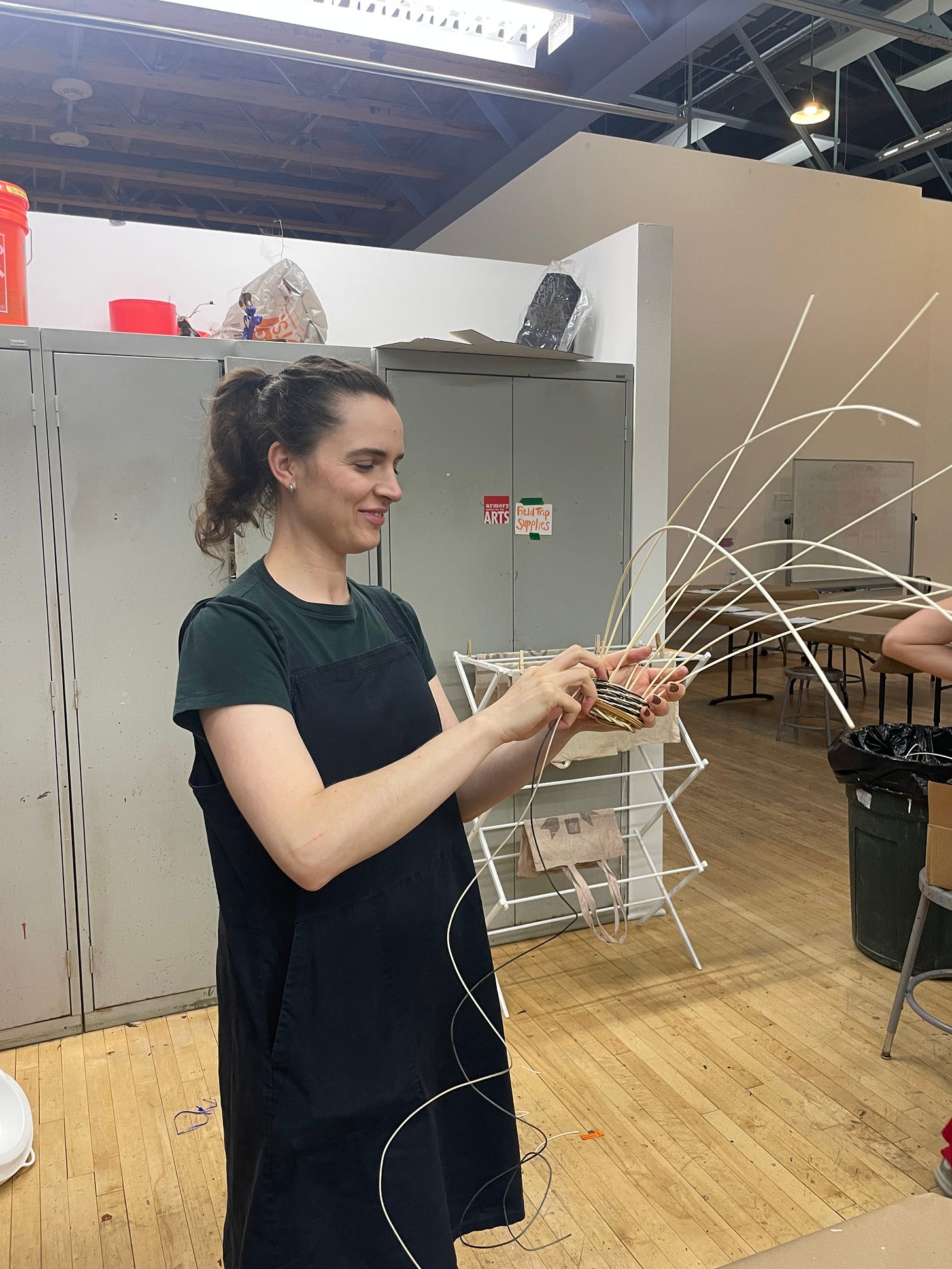 Woman in a classroom weaving a small basket while standing