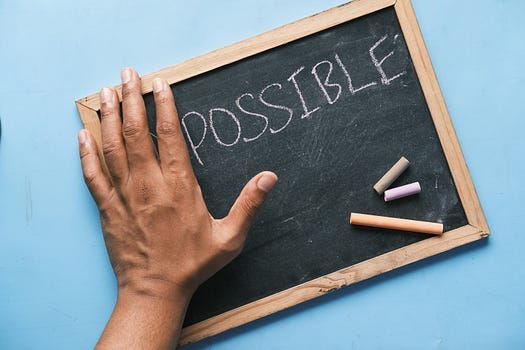 The word “POSSIBLE”, written with white chalk on a small black board.