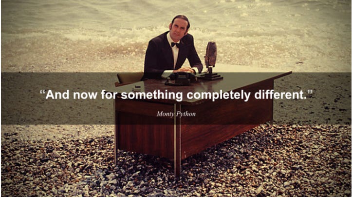 A man in a suit with a bowtie sits at a desk on top of a pile of rocks, the white words "and now for something completely different" are superimposed on the screen