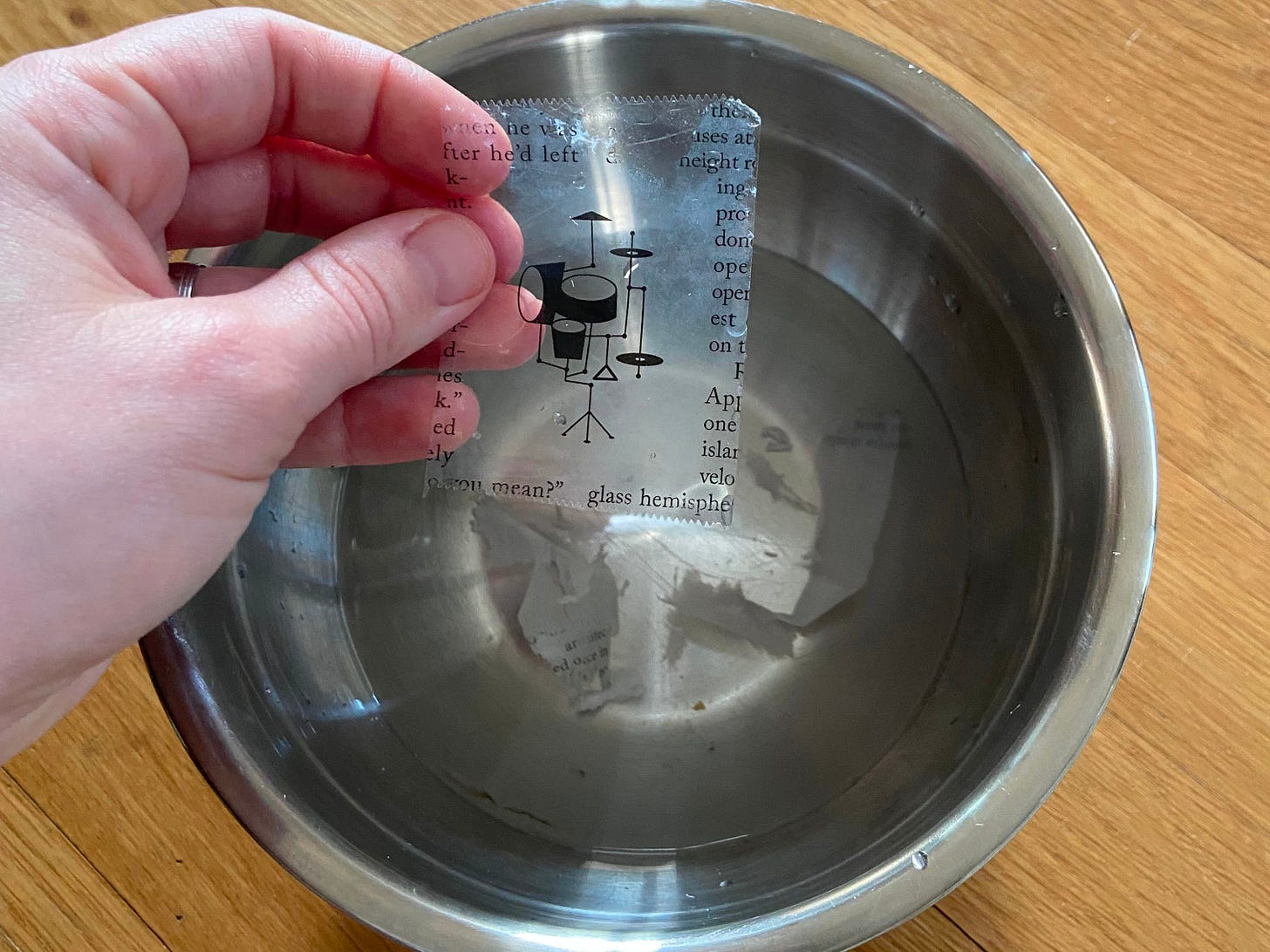 a hand holding a piece of tape with an outline of the drum set, hovering above a bowl of water