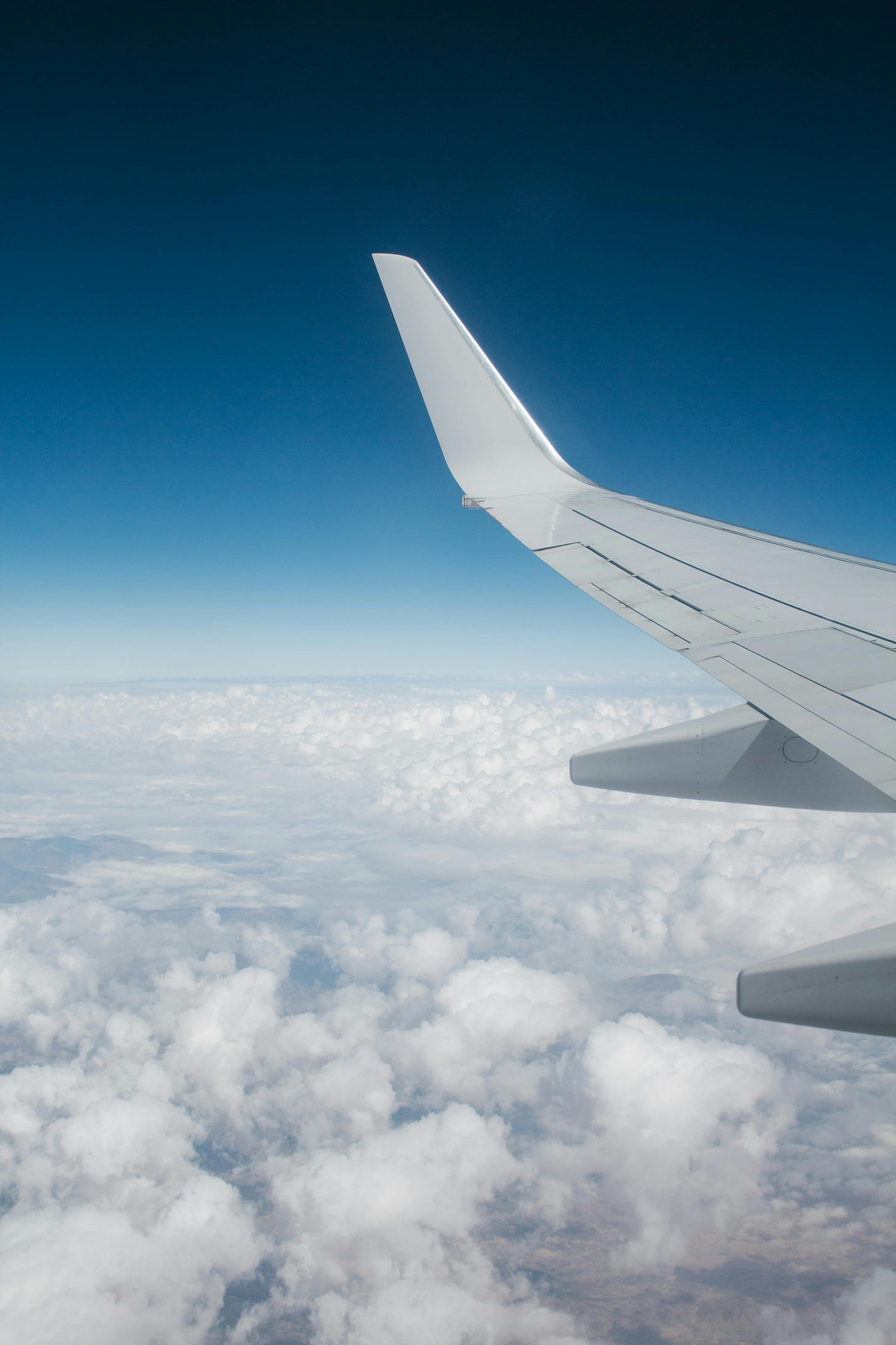 blue sky and clouds, with plane wing shown from plane seat window.