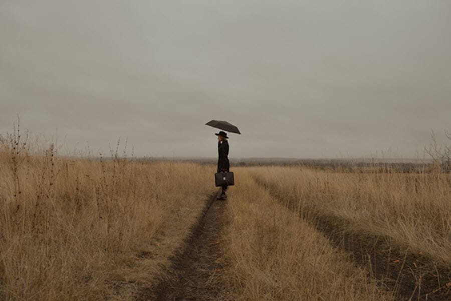 woman on a journey in a field with an umbrella and suitcase