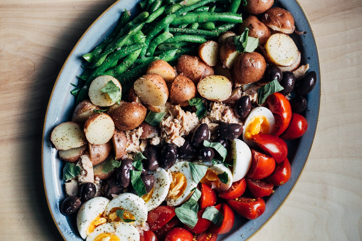 A platter with a variation on salad nicoise, including green beans, potatoes, tuna, olives, eggs, and tomatoes.
