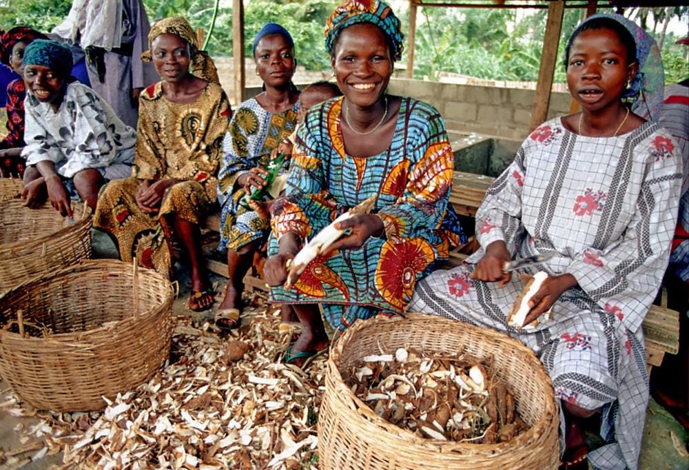Women cassava farmers in Nigeria sit at their farm on a bench chatting