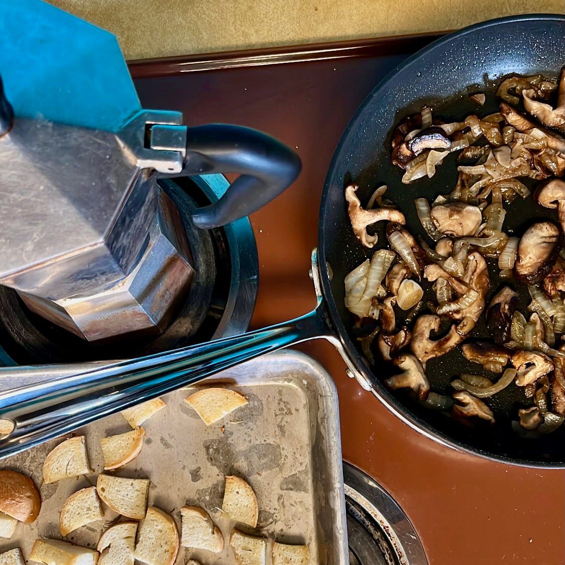 the top of my stove, with a pan of croutons in the bottom left and a pan of sautéed mushrooms and onions in the top right. my moka coffee pot is in the top left.