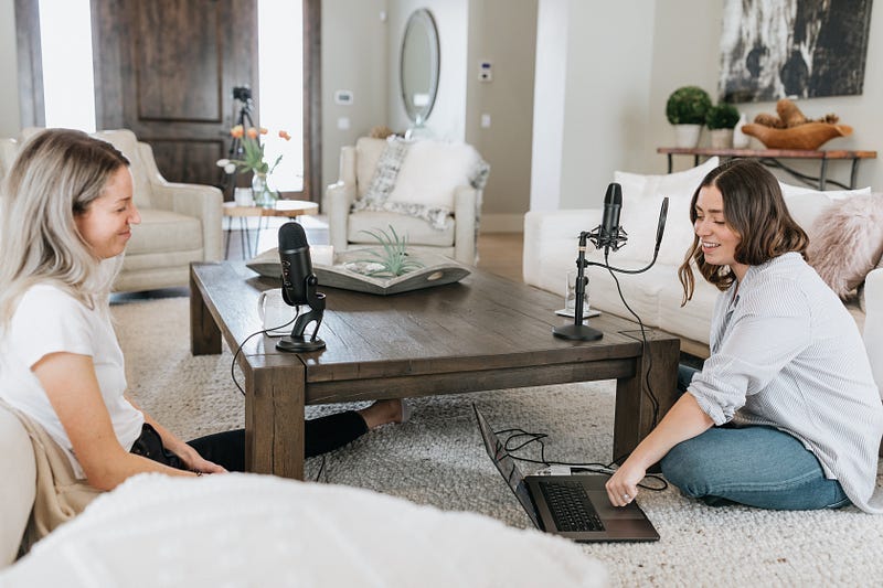 Two women sitting on floor making a podcast.