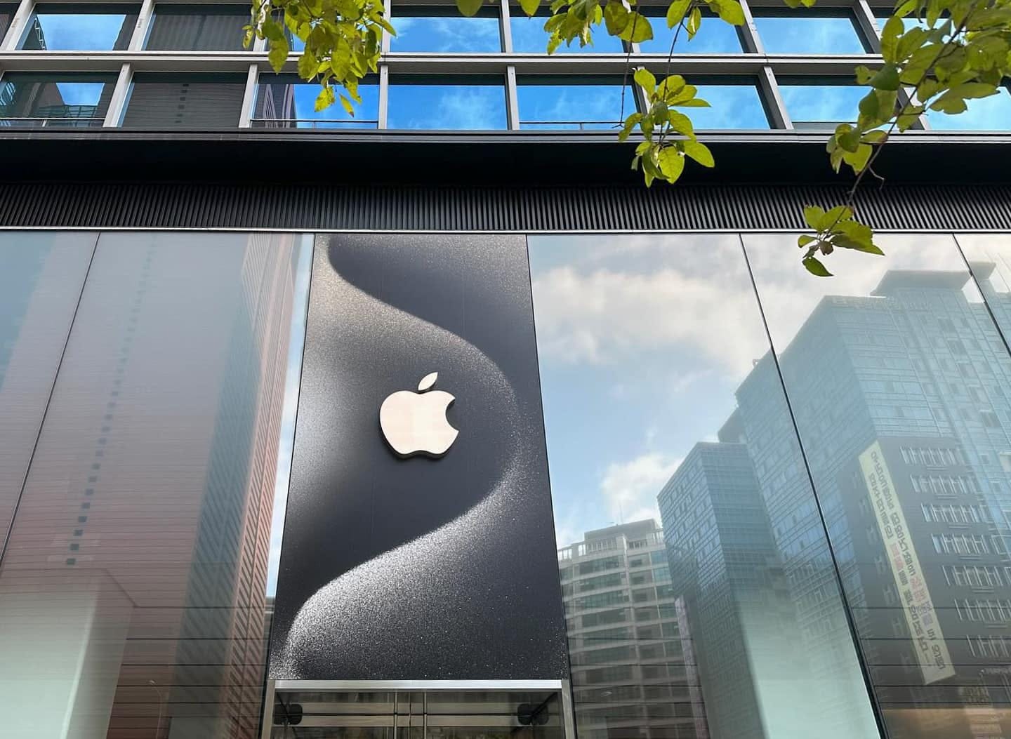 The facade of Apple Gangnam. Above the door, one pane of glass is covered with a decal that mirrors the iPhone 15 Pro wallpaper image. 