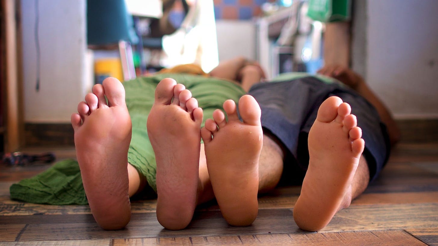 Two people lying on the floor of a house from the perspective of the bottom of their feet