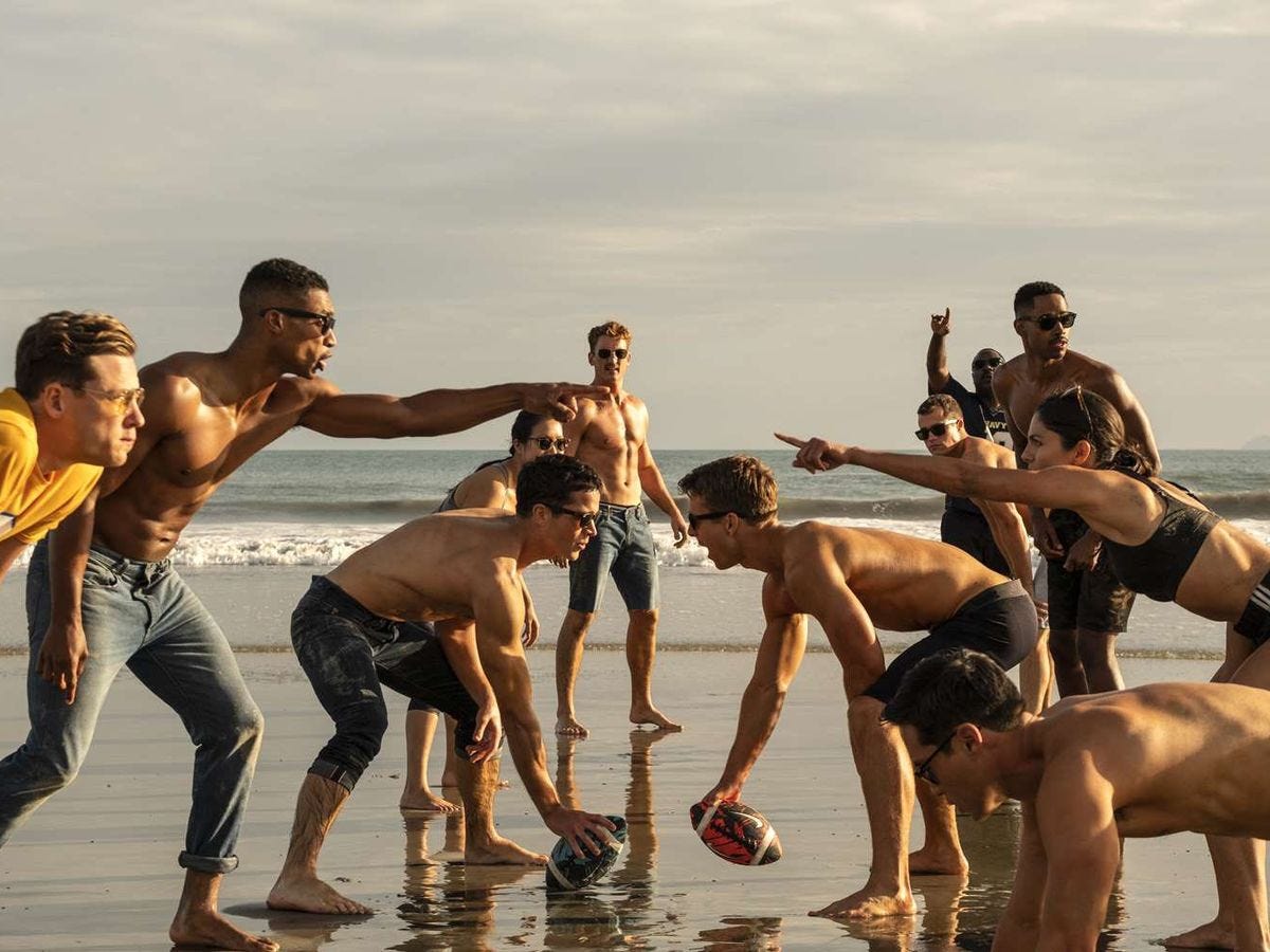 The cast of Top Gun: Maverick playing beach football. Two people pointing at each other across the line of scrimmage.