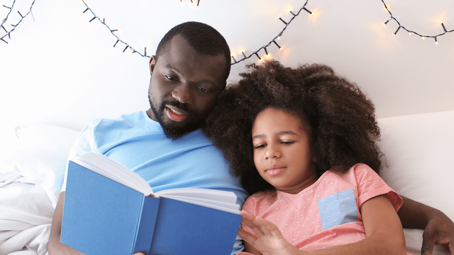 Father reading a bedtime story from a book to his daughter.