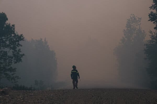A man in firefighting gear walking a desolate road surrounded by smoke.