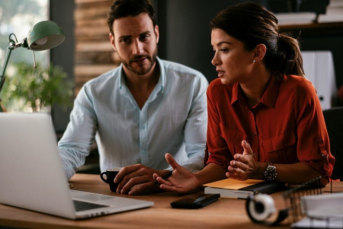 A man and woman talking in front of a computer.