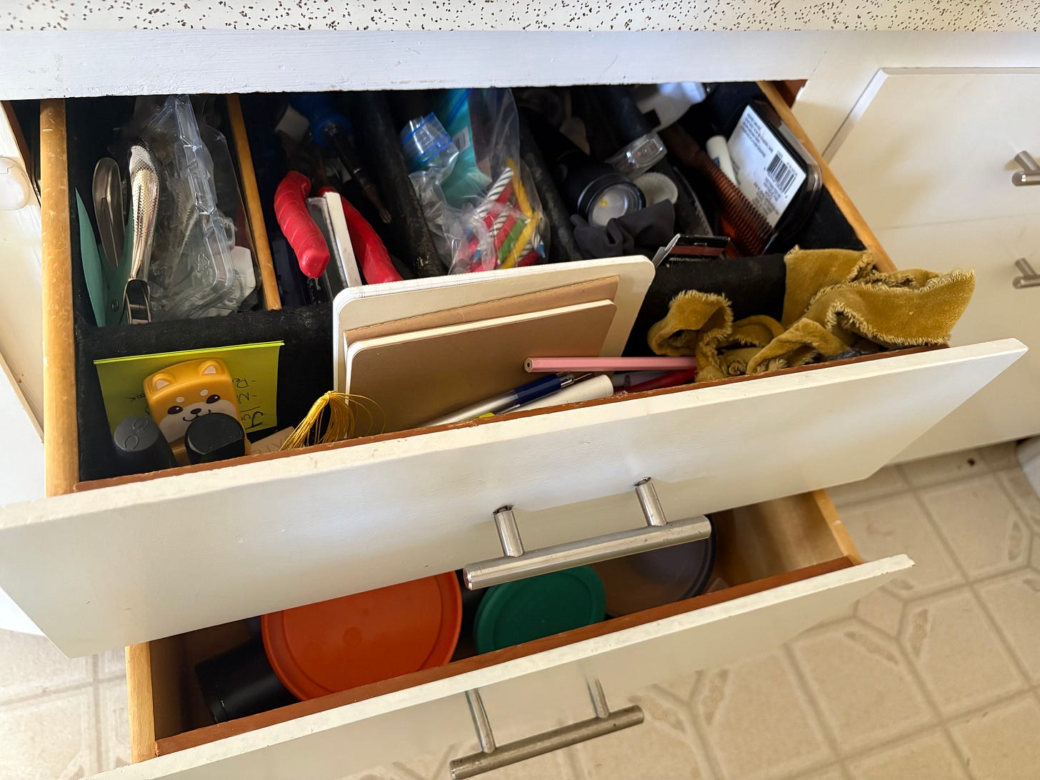 A half-open junk drawer, with miscellaneous house-hold items filling every compartment.