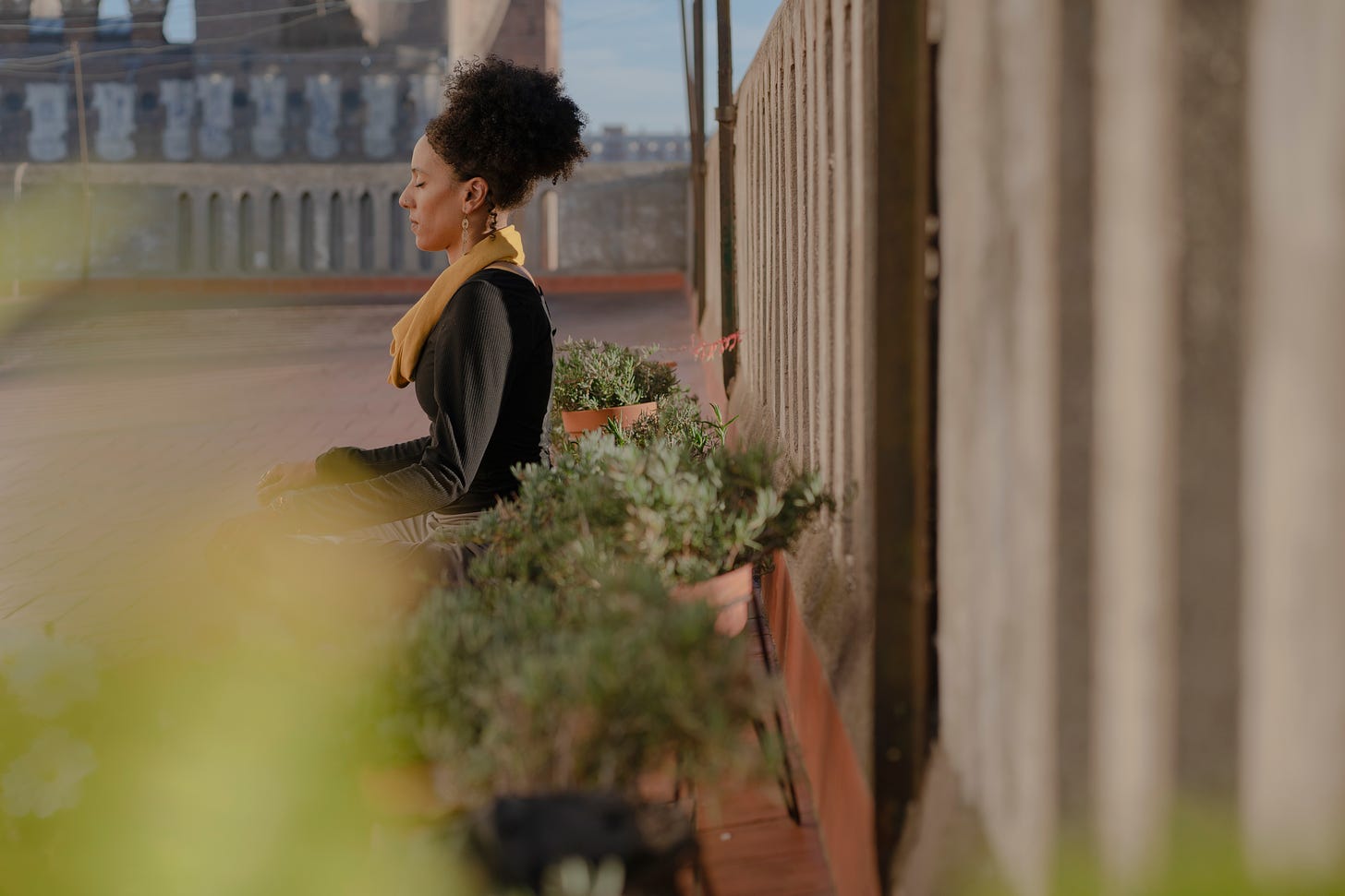 A black woman seated doing a grounding meditation on a rooftop terrace