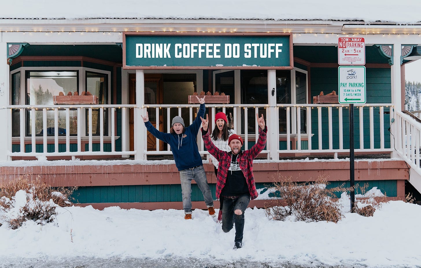 Standing in the snow in front of coffee shop, three stocking cap clad friends throw up the rock n roll devil horns in excitement.
