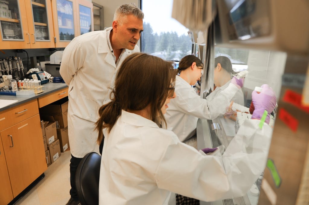 Jonah Sacha, Ph.D., senior co-author of a study published today in the journal Nature Communications, says new research could lead to a universal influenza vaccine withing five years. Sacha standing in his lab watching two lab workers do hood work. (OHSU/Christine Torres Hicks)