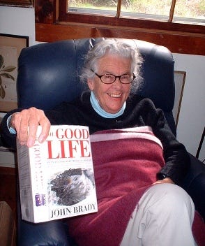Mrs. Ferguson, holding up the book THE GOOD LIFE, while sitting in a chair and smiling for the camera