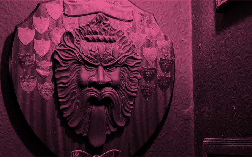 A shield with a grimacing Green Man on the wall of a pub.