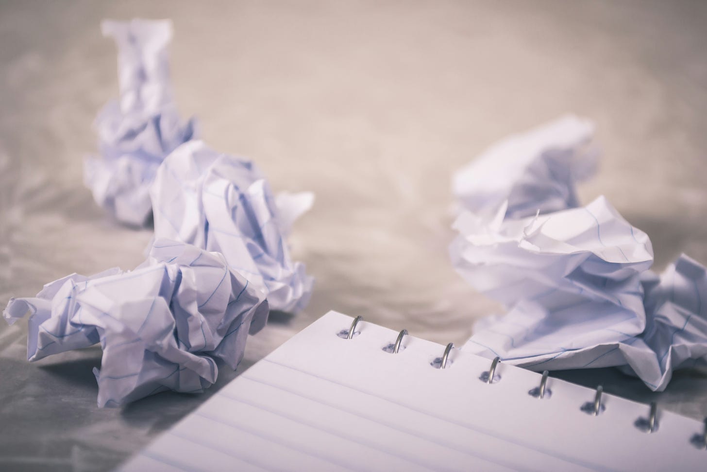 Pieces of balled-up paper are scattered on a white surface, along with a spiral-bound notebook.