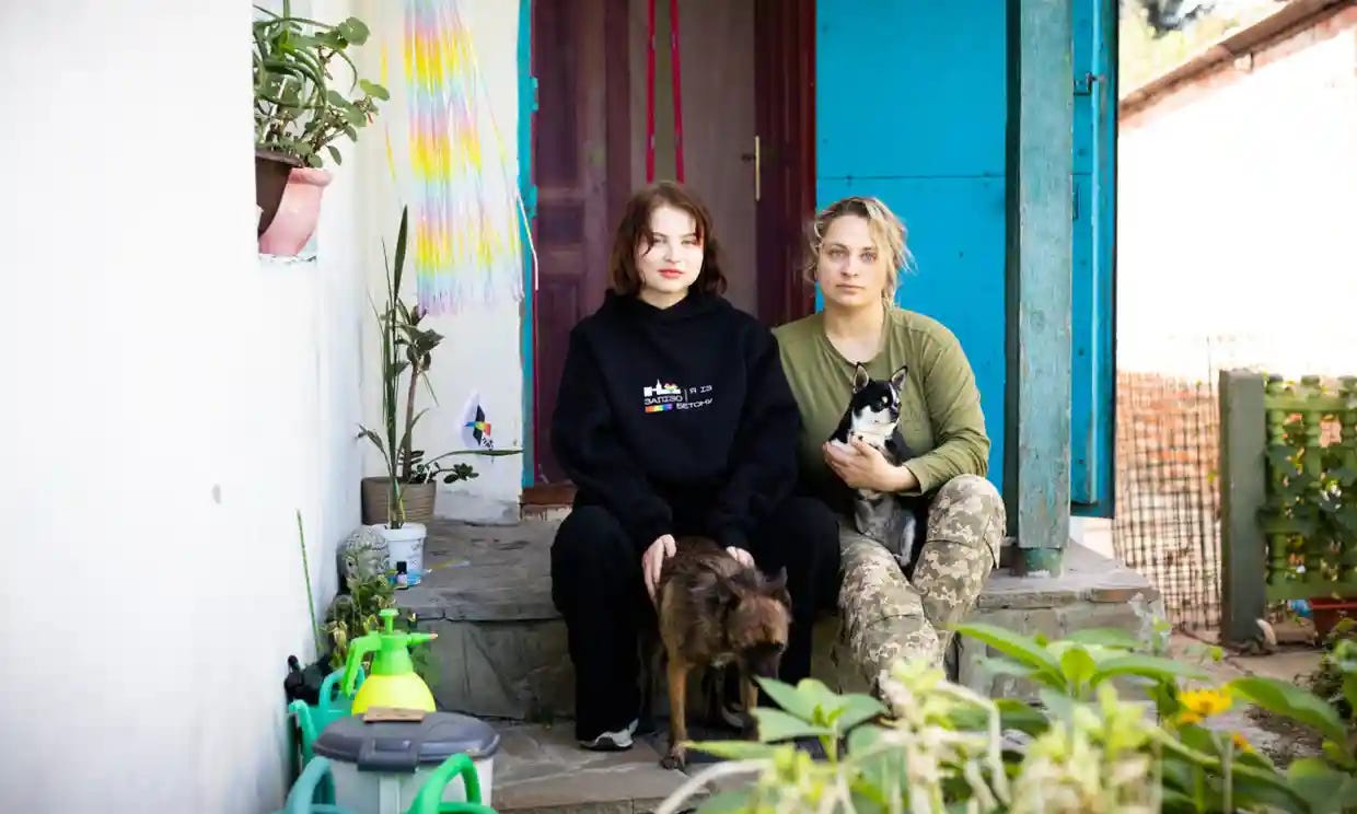 Two women sitting on a porch with a dog and a cat Description automatically generated