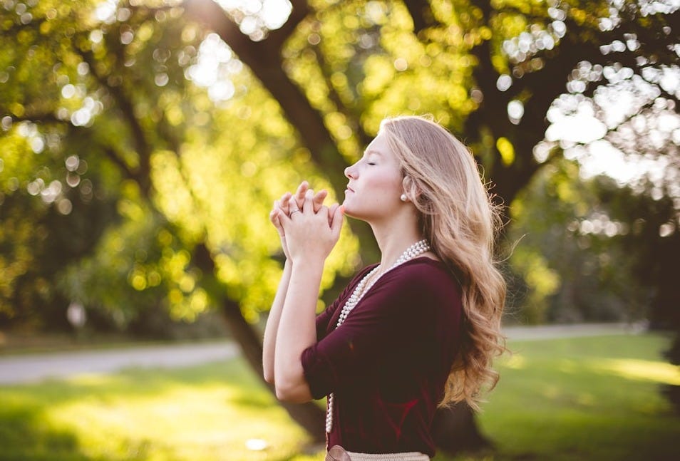 woman praying under tree during daytime