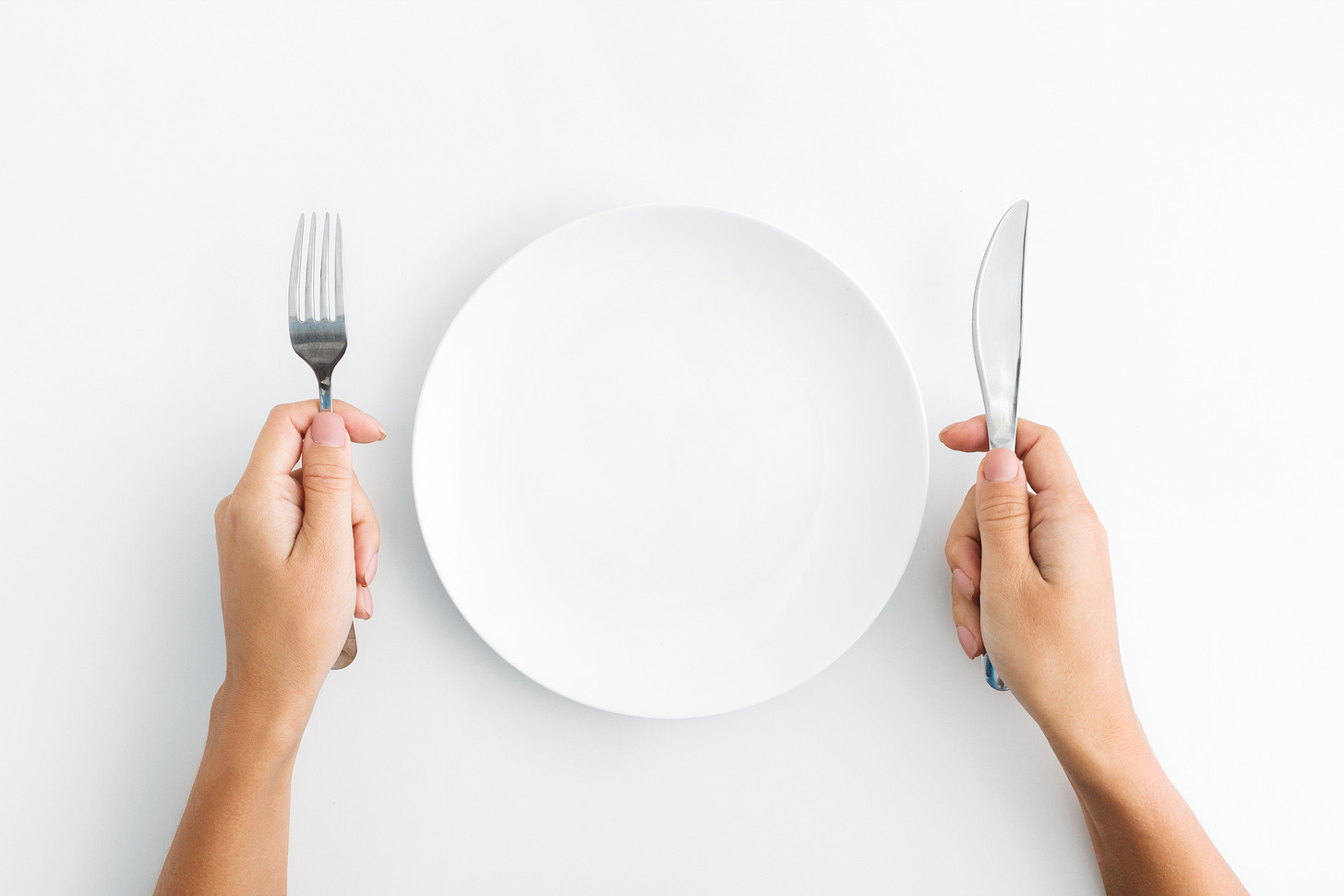 A picture of a person holding a fork and a knife with an empty plate in front of them