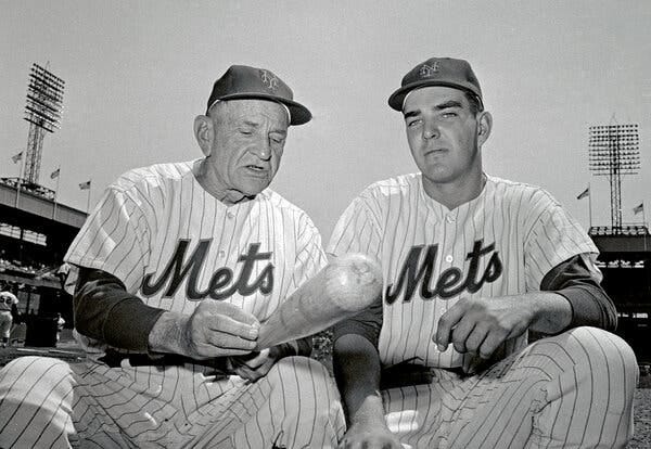 A black and white photo of Kranepool sitting alongside Casey Stengel, who is holding a bat and talking.