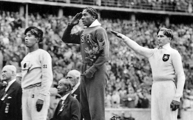 America's Jesse Owens, center, salutes during the presentation of his gold medal for the long jump, alongside silver medalist Luz Long, right, of Germany, and bronze medalist Naoto Tajima, of Japan, during the 1936 Summer Olympics in Berlin, August 11, 1936 (AP Photo/File)