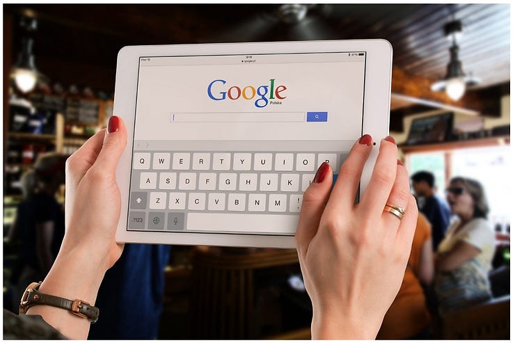 A woman's hand holding a tablet on which google search page is open