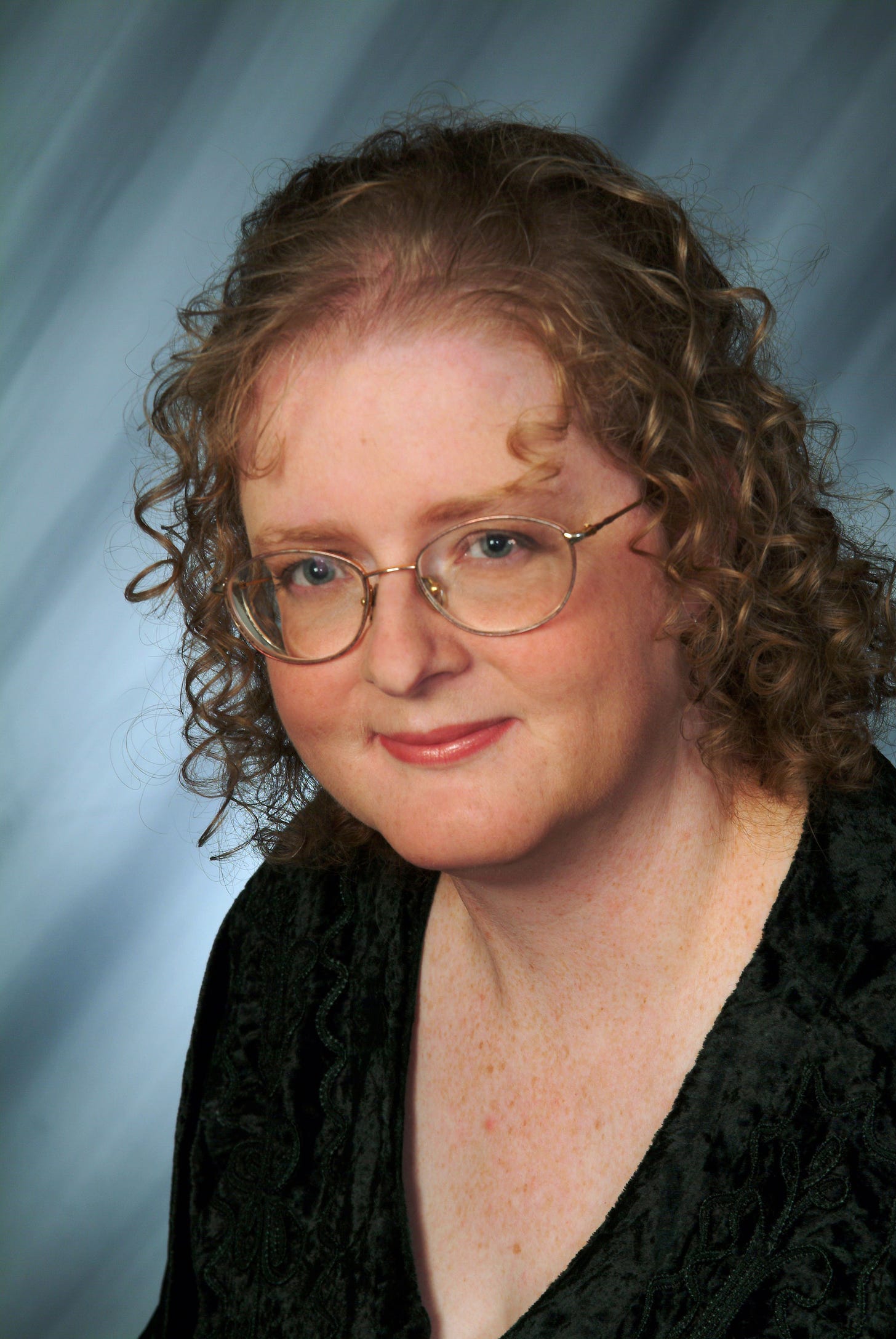 photo of author wearing glasses and immaculately styled hair and makeup against a blue streaky background