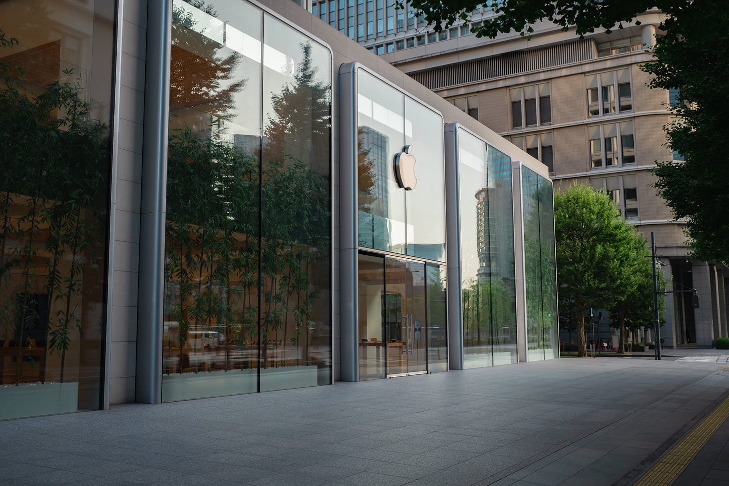 The exterior of Apple Marunouchi, shot from a low angle. Trees reflect in the glass.