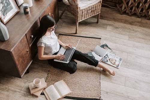 Free Casual home workspace with a woman using a laptop, surrounded by books and magazines. Stock Photo