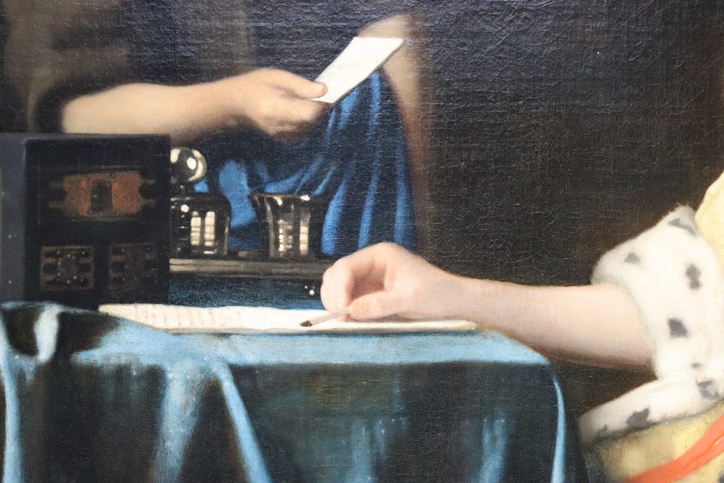 A section of a vermeer painting in which a woman sets down a quill pen while another extends a folded note  towards her.