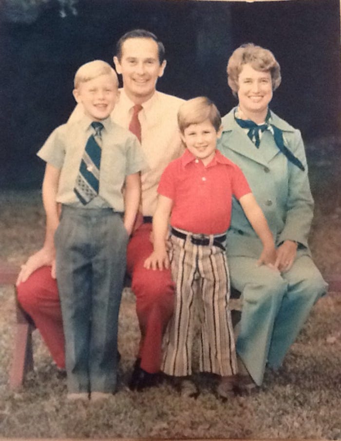 A color photo of a family of 4: a man in a red tie, a woman in blue, two young boys.