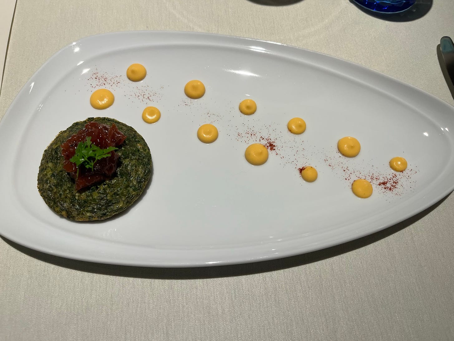 Green herbal omelet with red jam and an herb on top, with dots of yellow sauce on the side