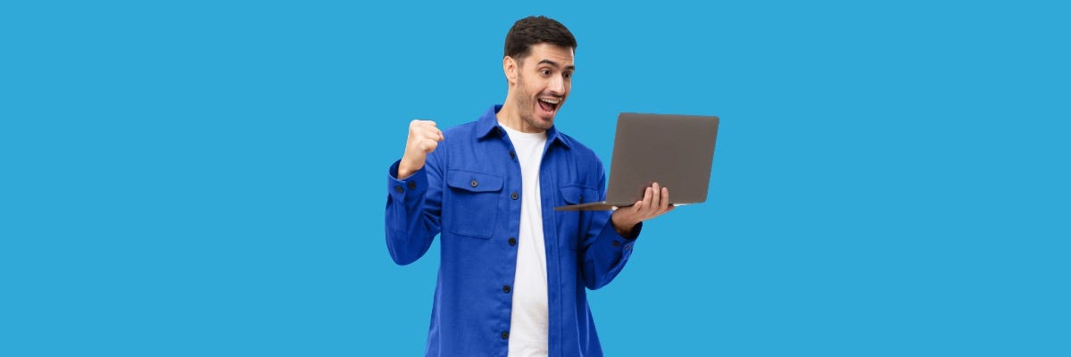 Excited man in a blue shirt celebrates while holding a laptop, against a solid blue background.