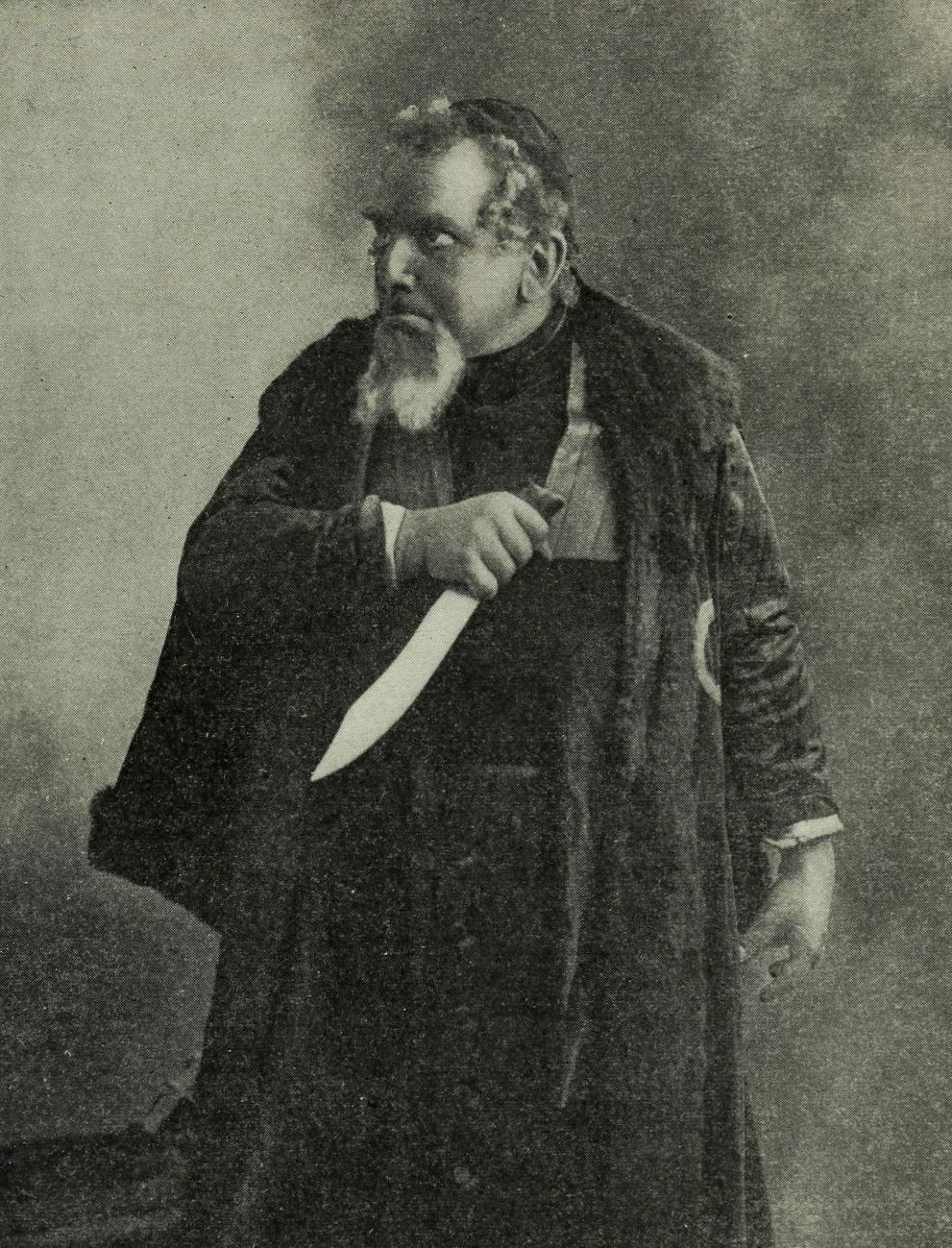 black and white early 20th century photo of actor plyaing Shylock; in period robes holding a knife