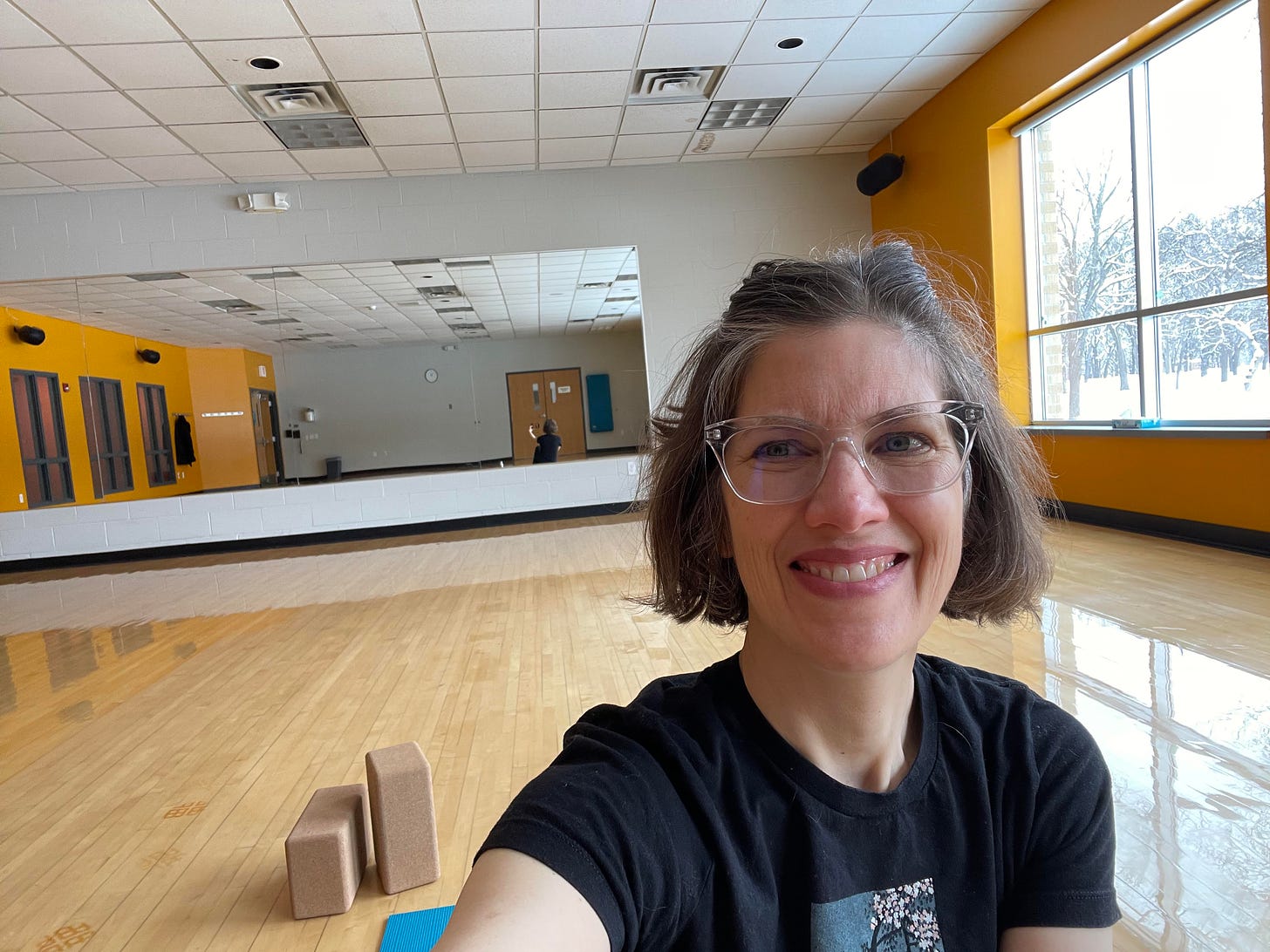 A smiling woman sits in an empty yoga studio