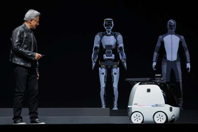 Jensen Huang walking toward a little white robot vehicle with two humanoids in the background